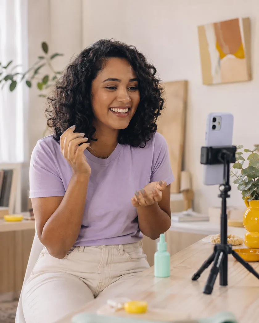 Creator sorrindo enquanto grava um vídeo de skincare com o celular em um tripé, em casa